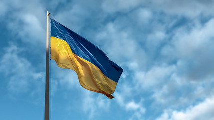 Blue and yellow Ukrainian national flag on a flagpole against a blue sky in the sunny day, view from below, blurred background. elections in Ukraine 2019.