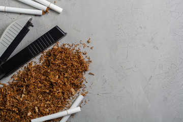 Making cigarettes with tobacco rolling machine on a gray stone table, top view, copy paste place