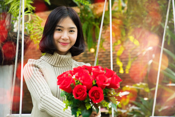 Portrait of a young beautiful woman smelling and holding red rose flowers in park