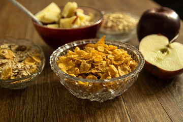 Corn flakes in a crystal bowl, fresh red organic apple and other healthy food on wooden table