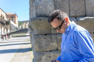 A man with black glasses checks something while walking next to a wall