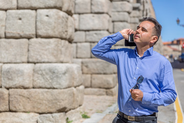 Obraz premium A businessman speaks on the mobile phone, and in the other hand wears black glasses, while walking through an old part of the city