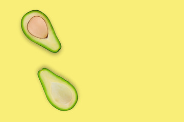 Fresh halves with and without kernel of organic avocado on yellow table in kitchen or market. Top view. Cooking concept. Copy space for your text