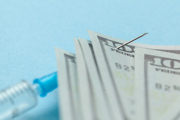 Syringe and paper dollars pinned to needle on blue background. Expensive medical insurance