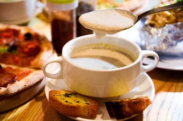 Bowl on a table with mushroom soup and a spoon hovering above