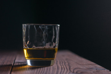 Close-up whiskey glass on the edge of a wooden table with a dark background at the back