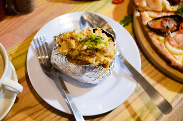 Woman eating baked mash potato wrap with aluminium foil. Lunch, dinner at restaurant