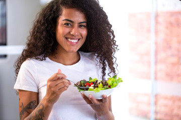 cheerful young afro american woman eating vegetable salad in home kitchen 