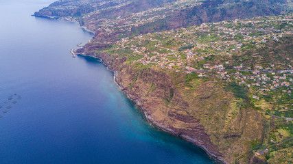 Obraz premium Aerial panoramic cityscape view of the cities in madeira with houses in front and covered mountains and white clouds