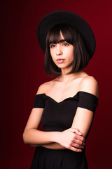 Young fashion woman with black hat standing isolated on red background