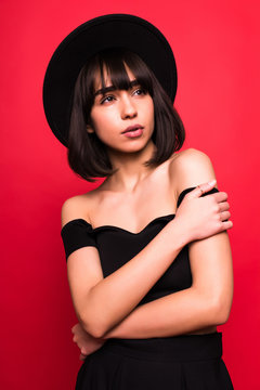 Young brunette woman in fluppy black hat and black clothes on red background