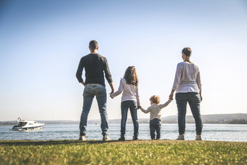 All family together holding hands near the sea. Four people standing on the seashore in a beautiful sunny day. Mother, father and two daughters looking at the horizon. Concept of friendship and union