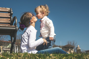 A tender kiss from two little sisters playing together on a sunny day at the park. Concept image of friendship, brotherhood and family love. A couple of young girls kissing eachother enjoying outdoors