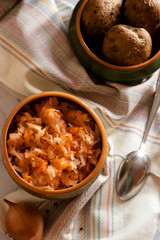 sauerkraut with boiled potatoes in earthenware on a light background