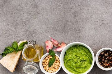 Pesto sauce with ingredients garlic, basil, pine nuts on a neutral grey background. Copy space.