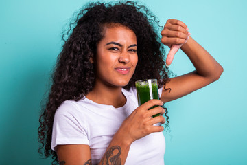 Disgusted africanwoman tasting a vegetable juice with bad flavor on green background