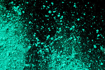 A splatter of green blue colored pigment powder on black background.