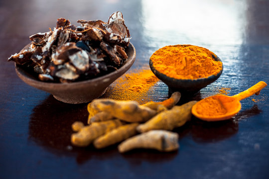 Tamarind or imli or amli in a clay bowl along with its roasted seeds on wooden surface with turmeric or haldi in a clay bowl used for treating acne and pimple.