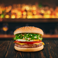 burger with cutlette and omlette at wooden tabletop with blurred bar at backdrop . Fastfood advertising concept.