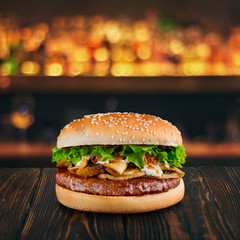 burger with mushrooms at wooden tabletop with blurred bar at backdrop . Fastfood advertising concept.