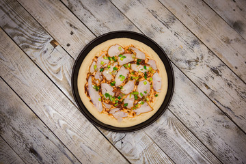 Round pizza dough is in the pan. The process of cooking pizza, stacking ingredients on the dough.