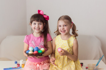 girls sisters 6-7 years old twins with dark and blond hair consider and show easter eggs