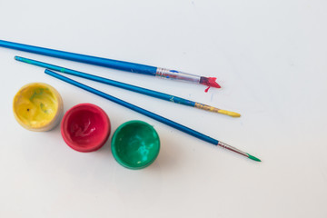 Three cans of gouache paint, red, green and yellow next to the brushes