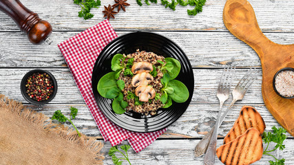 Quinoa with spinach and mushrooms. In a black plate on a wooden background Top view. Free space for your text. Flat lay