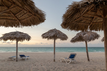 Empty beach with deckchairs and palm leaves umbrellas. Vacation concept