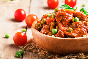 Ragout with beef, carrots, green peas and tomatoes, old wooden background, selective focus
