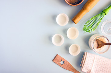 Culinary background. Cooking utensils, a whisk, a rolling pin, cupcake pans, a wooden bowl and baking ingredients. Bakery background frame. Top view, copy space.