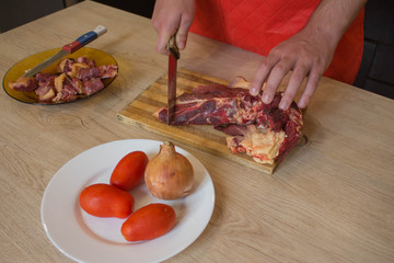 Man cuts of fresh piece of meat on a wooden cutting board in the home kitchen