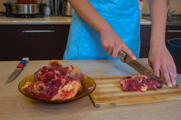 he is cutting meat or steak for a dish on wooden board. Preparing meal