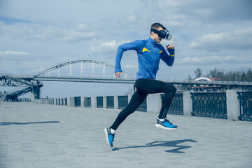Man running on city background. Handsome athlete using VR glasses while runnig at morning. Healthy lifestyle and high tech concept.