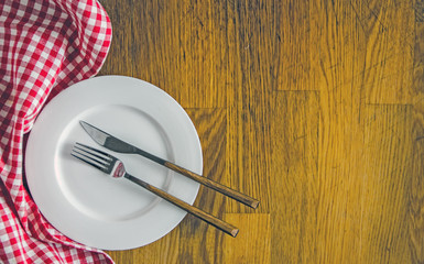 Red checkered dishcloth, white plate and cutlery on wooden background. Culinary background. Table...
