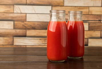 Two bottles with tomato juice on a dark wooden table.
