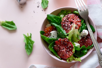 Spring fresh salad with blood orange, lettuce, spinach and sesame seeds on pink background. Top view. Selective focus