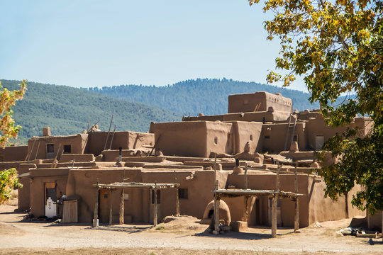 Multi-storied adobe mud Native American pueblo dwelling in the Southwestern United states with drying racks and outside ovens with mountains in the distance - selective focus
