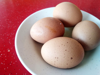 Four boiled eggs are placed on white plates. Placed on a red table.