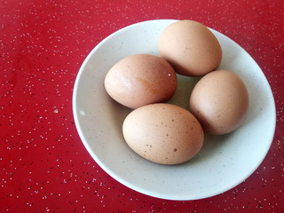 Four boiled eggs are placed on white plates. Placed on a red table.