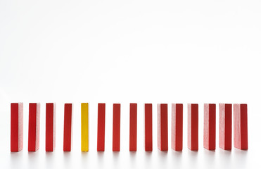 Yellow wooden block between row of red ones on white