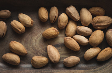 Dark photo of pistachios nuts in wooden dish. Illuminated Pistachios in wooden bowl.  Stack of bio pistachios - top view photo.
