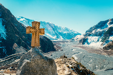 Amazing view alongside Georgian military road, high in the Caucasus mountains. Winter time, high mountain peaks covered with snow. Wooden cross beside the road.