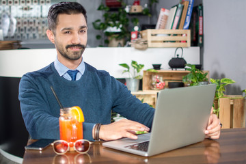 Smiling young man in business wear using laptop in a cafe