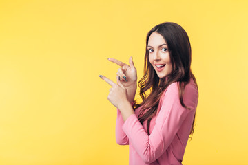 Beautiful smiling woman showing empty copy space pointing her fingers isolated on yellow background