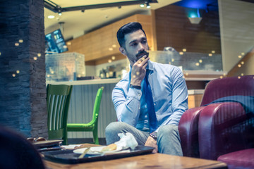 Portrait of handsome young businessman with hand on chin and pensive expression relaxing after having a meal in cafe during office break.