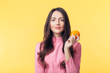 Beautiful young woman holding orange in hand isolated on yellow background