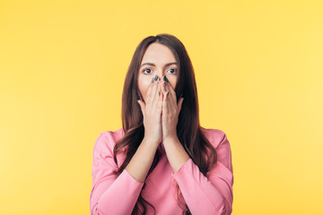 Shocked excited woman covering her mouth with hands on yellow background