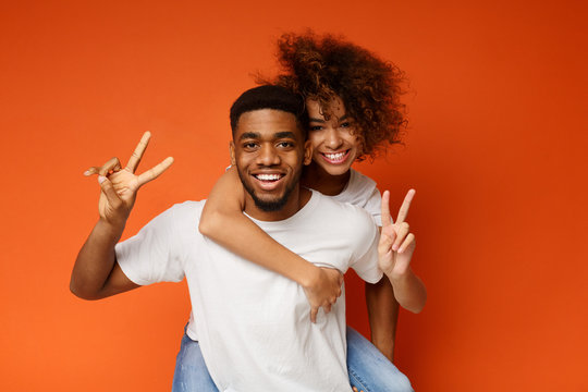 Cheerful black couple piggybacking on orange background
