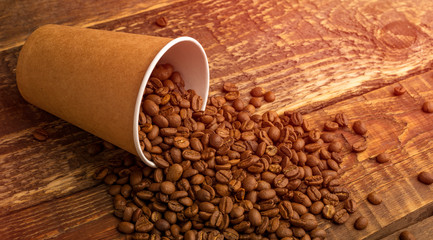 Disposable cup Kraft with coffee beans scattered on the wooden table. copy space for text